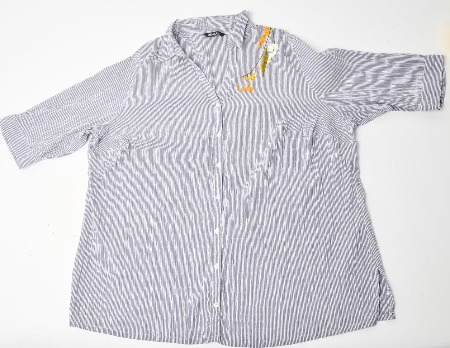 Flat image of an oversized blue and white striped seersucker top placed on a white background. Pochoir.NYC embroidered the left shoulder with orange, white, and gold blossoms.