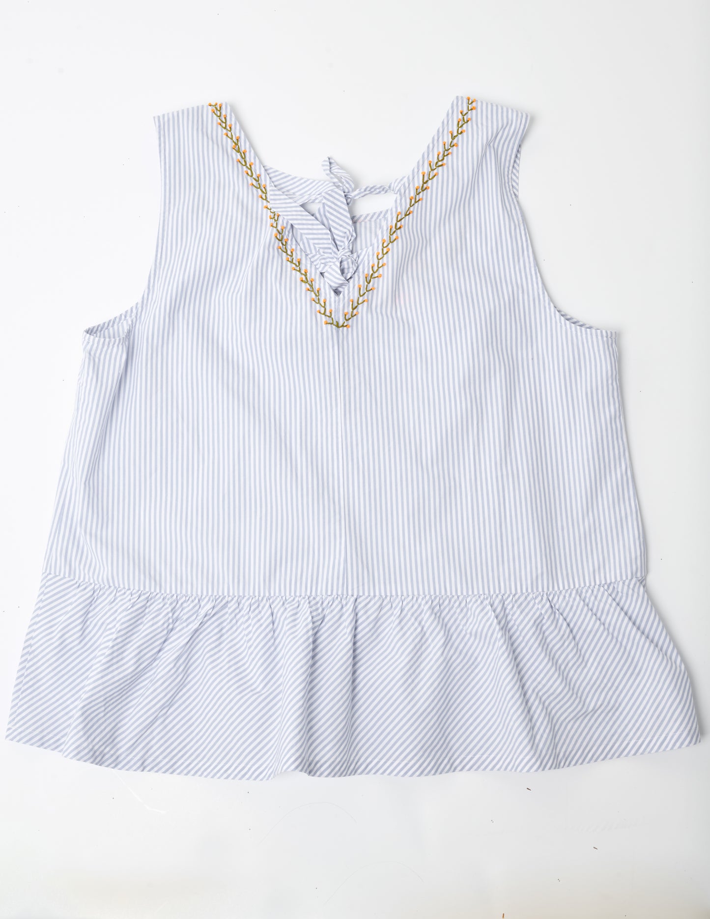 Closeup image of a blue and white striped sleeveless top with a peplum at the hem. The top is turned to the back so the viewer can see that there the back neckline is a deep V neck with ribbons tying it closed. Pochoir.NYC stitched the back neckline with small orange blossoms.