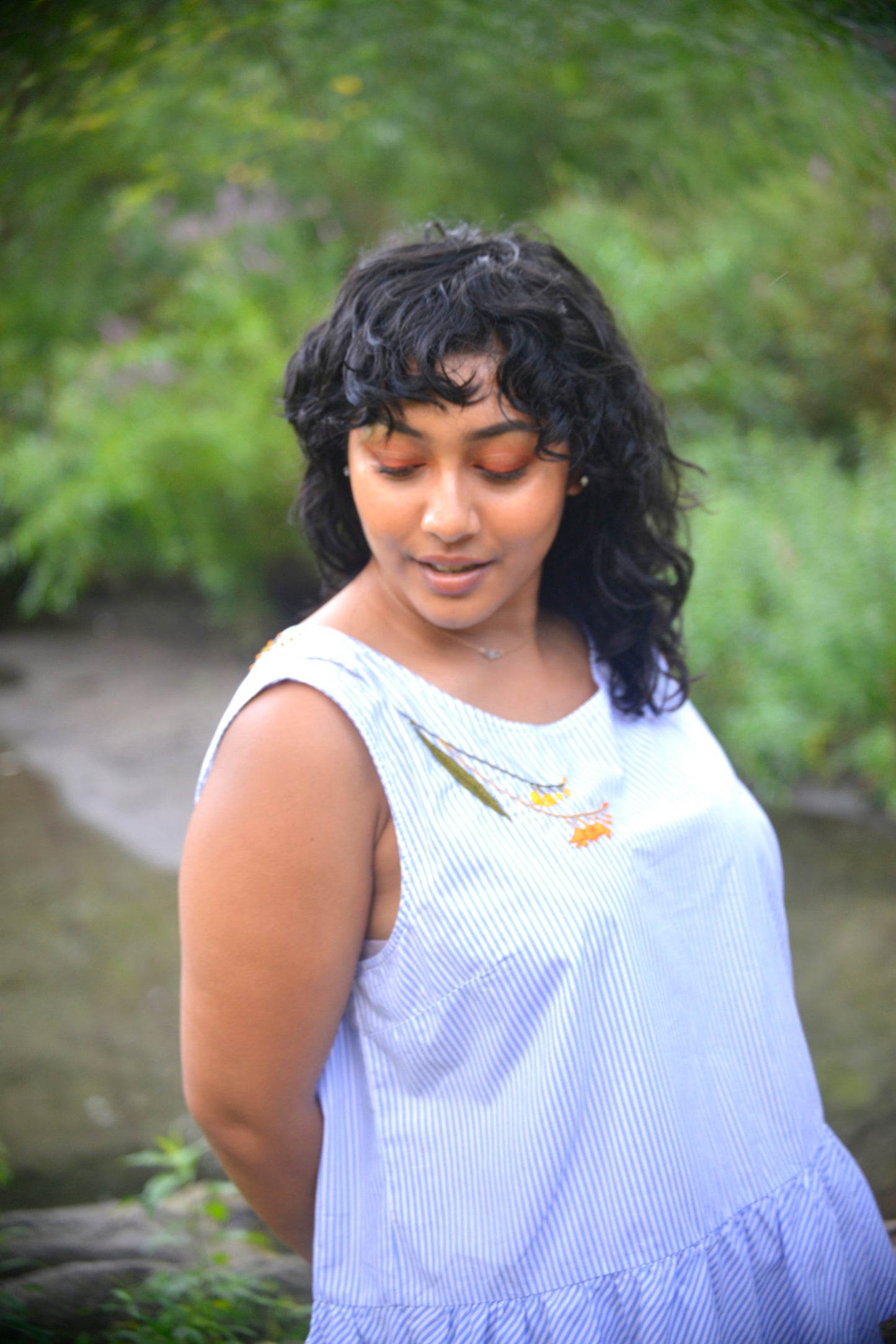 Model with dark hair and brown skin wears a blue and white striped peplum top hand embroidered by Pochoir.NYC with orange and yellow blossoms.