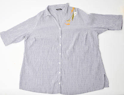 Flat image of an oversized blue and white striped seersucker top placed on a white background. Pochoir.NYC embroidered the left shoulder with orange, white, and gold blossoms.