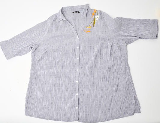 Flat image of an oversized blue and white striped seersucker top placed on a white background. Pochoir.NYC embroidered the left shoulder with orange, white, and gold blossoms.
