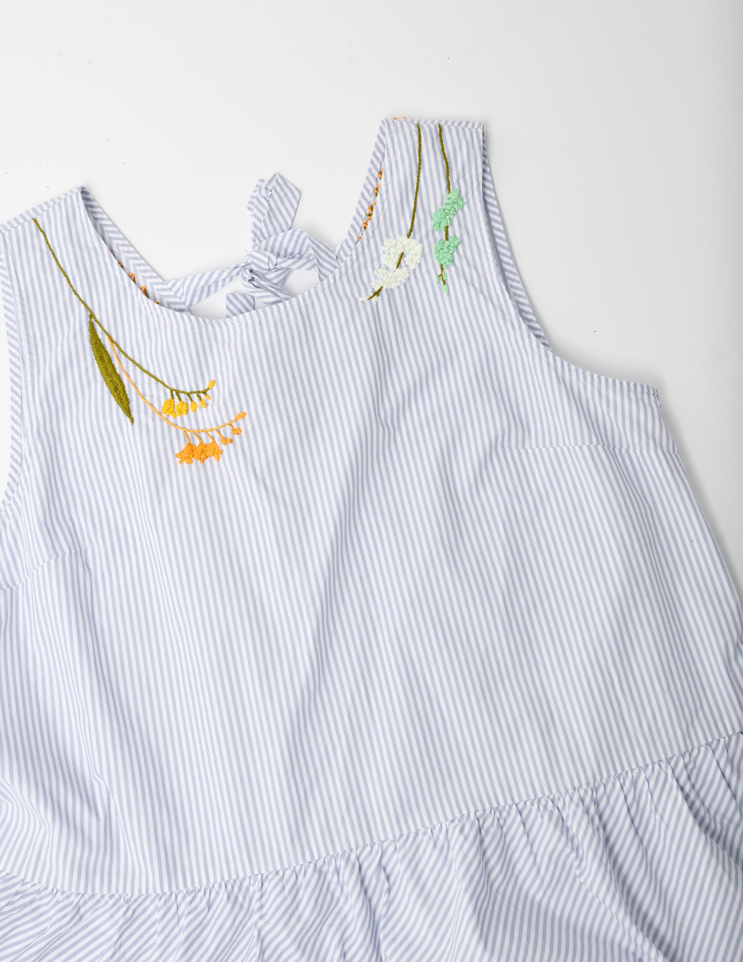 Closeup image of a blue and white striped sleeveless top with a peplum at the hem. Pochoir.NYC embroidered the neckline with orange, gold, white, and turquoise flowers.