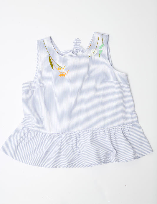 Closeup image of a blue and white striped sleeveless top with a peplum at the hem. Pochoir.NYC embroidered the neckline with orange, gold, white, and turquoise flowers.